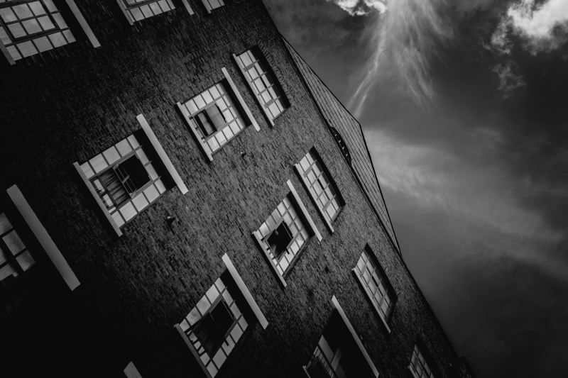 Black and white image of a converted industrial brick building in London with a clear sky and wispy clouds