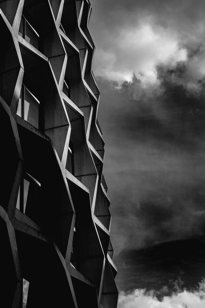 Portrait image in black & white of the concrete grid facade of Space House, (One Kemble Street), London. Mixed with the stormy cloud scene in the background - Architectural photography by Midi Photography